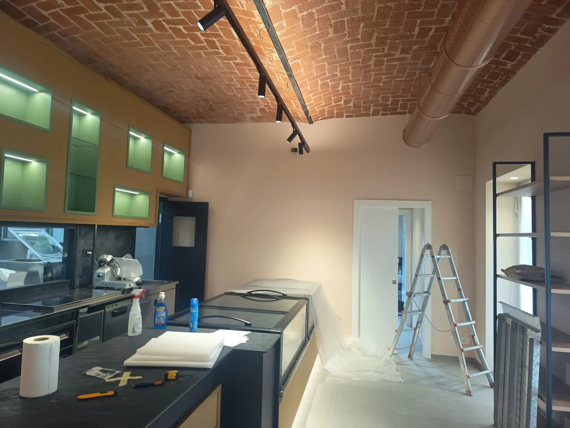 Cantiere di una cucina commerciale con soffitto a volta in mattoni a vista, pensili LED retroilluminati e finiture in fase di completamento