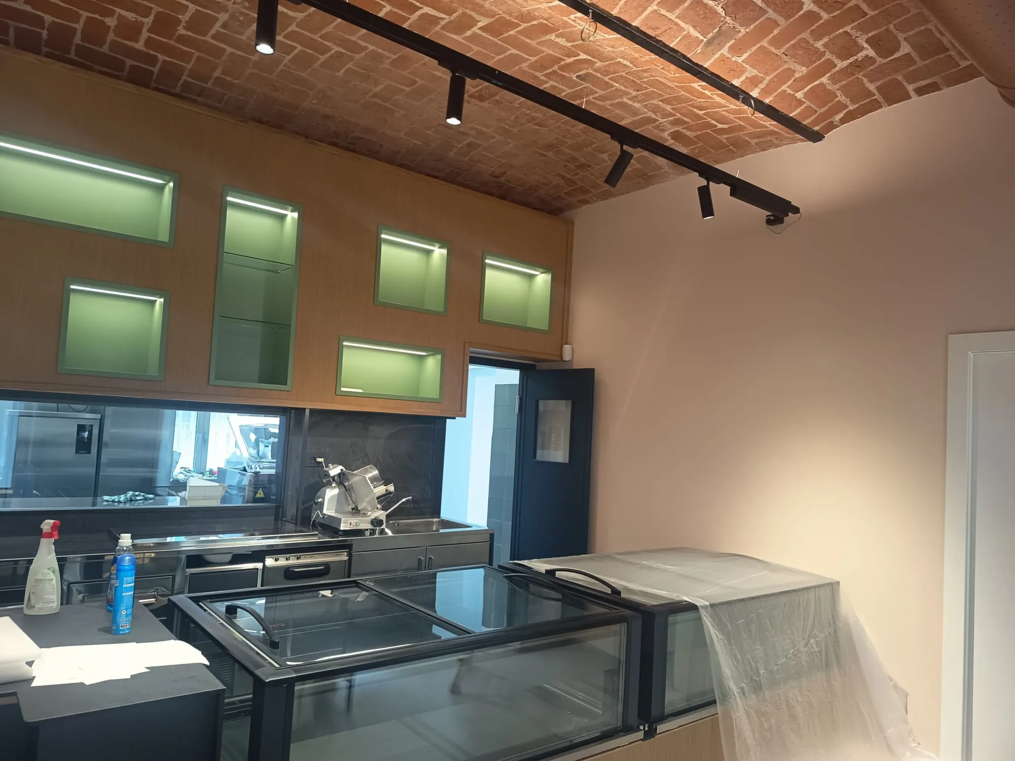 Cucina di un bar con pensili in legno e LED retroilluminati, soffitto a volta in mattoni a vista e finiture su misura