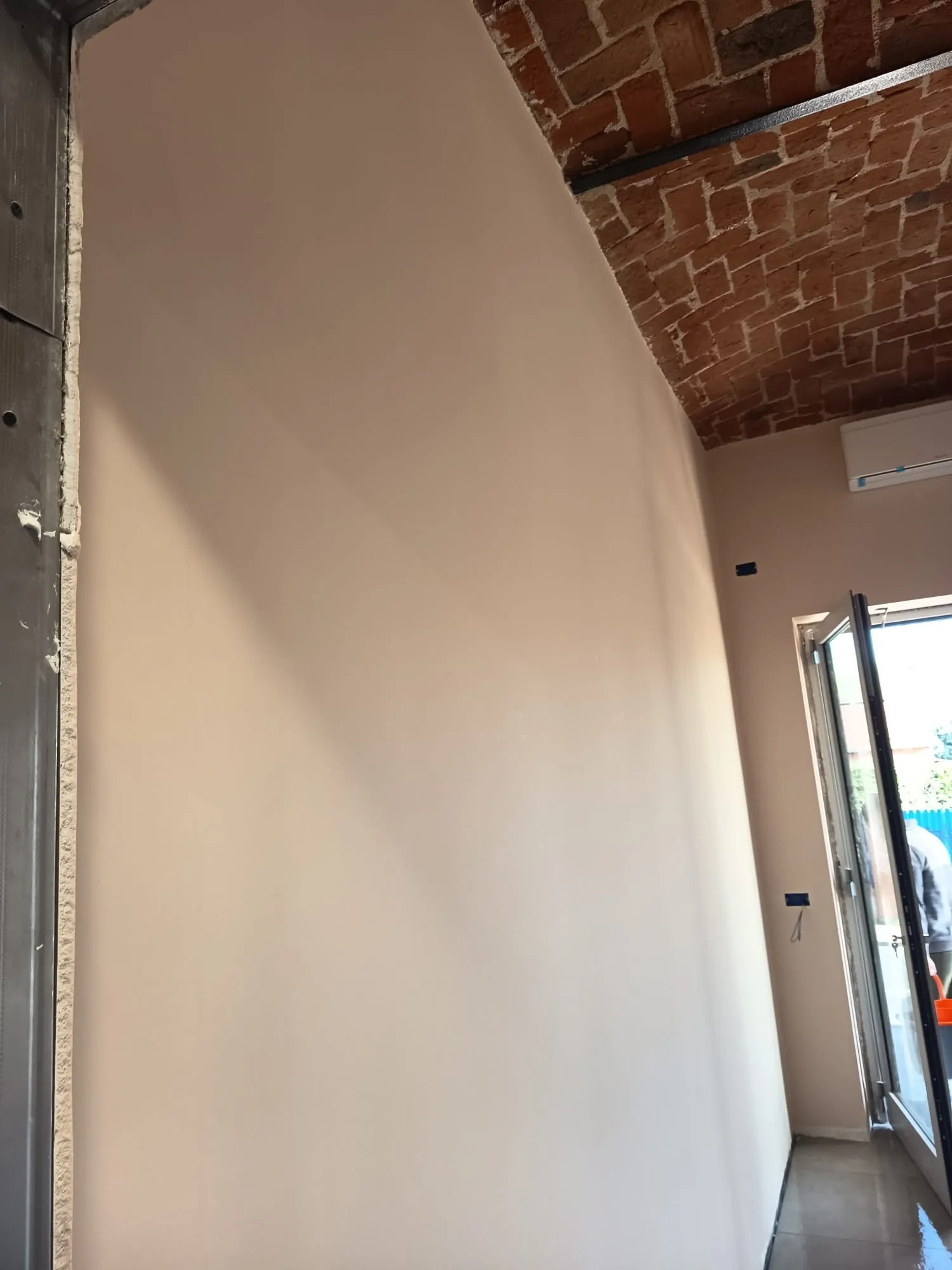 Parete decorata color avorio sotto un soffitto a volta in mattoni a vista