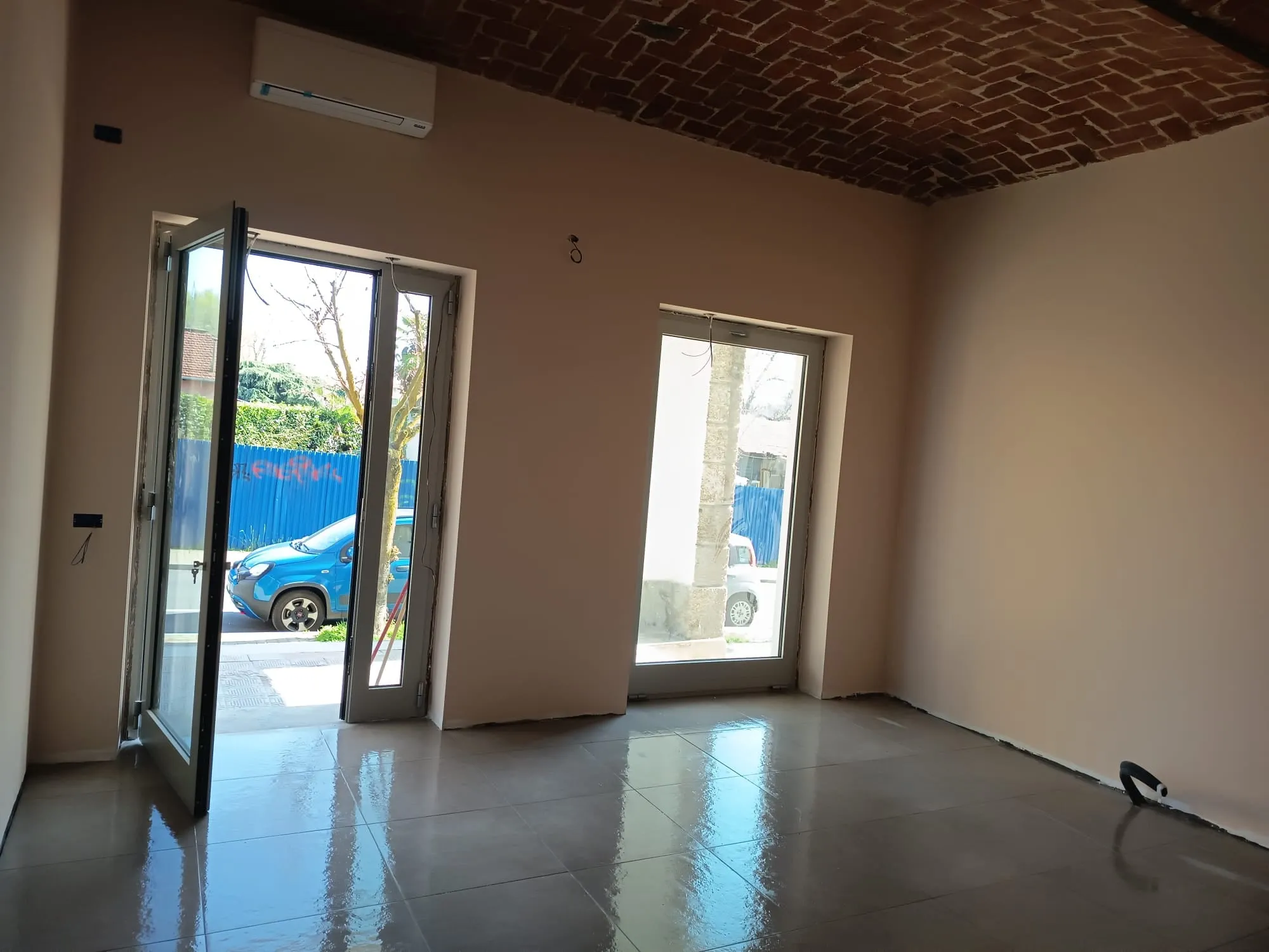 Ingresso di un locale commerciale con grandi piastrelle smaltate al pavimento, pareti color rosa cipria e soffitto a volta in mattoni a vista